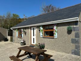 Exterior view of a single-story building with a white door two windows and a wooden picnic table outside at The Mill in Abererch near Pwllheli