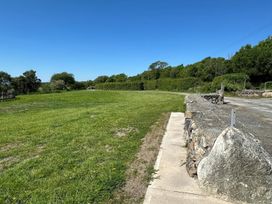 A grassy field with a stone wall and a dirt road under a clear blue sky at The Mill in Abererch near Pwllheli