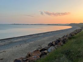 A curved sandy beach with rocks in the foreground and calm sea under a sunset sky at The Mill in Abererch near Pwllheli