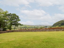 A grassy area with a stone wall and trees at Ty Gwyn in Llangwm near Bala