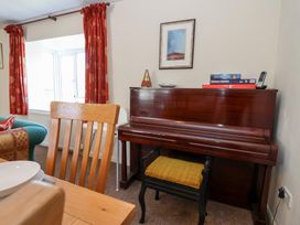 A room with a wooden piano and stool next to a window with red curtains at Moorside Horrabridge near Tavistock