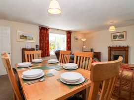 A dining area with a wooden table set with white dishes and cutlery in a living room with red curtains and a fireplace at Moorside in Horrabridge near Tavistock