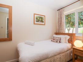 A bedroom with a single bed a pillow a rolled towel a bedside table with a lamp a window with curtains and a wall mirror at Moorside Horrabridge near Tavistock