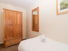 A bedroom with a wooden wardrobe a wall mirror a bed with a white sheet and rolled towel on it at Moorside in Horrabridge near Tavistock