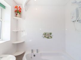 A bathroom with a bathtub white tiles a corner shelf with a flower vase and an electric shower at Moorside Horrabridge near Tavistock