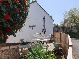 A small outdoor patio area with a white table and chairs set against a white wall with a metal dragonfly decoration and red flowers to the left at Moorside Horrabridge near Tavistock
