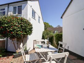 An outdoor patio area with a white table and chairs a bottle of wine and two glasses on the table surrounded by white buildings and greenery at Moorside in Horrabridge near Tavistock