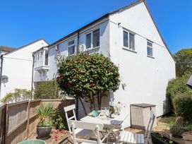 A small patio area with a white table and chairs next to a white house with a flowering tree and plants at Moorside in Horrabridge near Tavistock