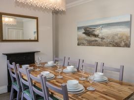 A dining room with a wooden table set with white dishes and glasses and purple chairs at Trevor Cottage in Llandudno