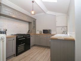 A kitchen with grey cabinets a black oven a microwave kettle and a sink at Trevor Cottage in Llandudno