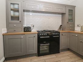 A kitchen with gray cabinets wooden countertops a black stove a toaster and knives at Trevor Cottage in Llandudno