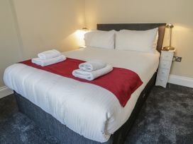 A bed with white linens and red runner with towels on the foot of the bed in a bedroom at Trevor Cottage in Llandudno