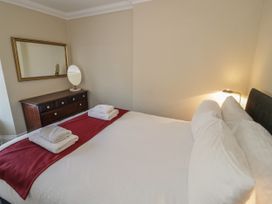 A bed with white bedding and red runner towels on a dresser with a mirror and round mirror on top at Trevor Cottage in Llandudno