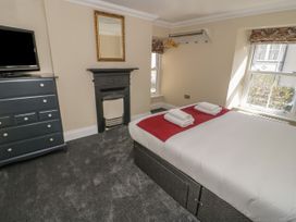A bedroom with a bed folded towels a black chest of drawers a television a decorative fireplace and two windows at Trevor Cottage in Llandudno