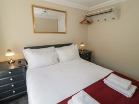 A bedroom with a double bed with white bedding and towels on a red blanket two bedside tables with lamps a wall mirror and a wall-mounted coat rack with hangers at Trevor Cottage in Llandudno