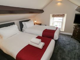 A bedroom with two single beds with red runners and white towels a bedside table with a lamp a window and a television on a chest of drawers at Trevor Cottage in Llandudno
