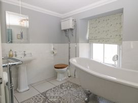 A bathroom with a pedestal sink mirror toilet clawfoot bathtub and window with bird patterned blind at Trevor Cottage in Llandudno