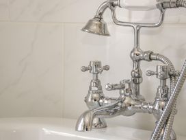 A close up of a chrome bathtub faucet and shower head against a tiled wall at Trevor Cottage in Llandudno