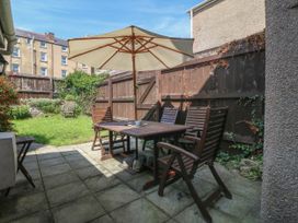 A patio with wooden table and chairs under an umbrella next to a grassy garden enclosed by a wooden fence at Trevor Cottage in Llandudno