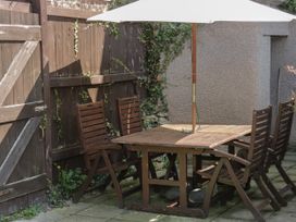 An outdoor patio area with a wooden table and four wooden chairs under a white umbrella surrounded by a wooden fence and wall at Trevor Cottage in Llandudno
