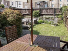 A garden with wooden patio furniture and a sun umbrella a small grassy area and a wooden fence at Trevor Cottage in Llandudno