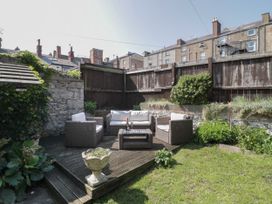 An outdoor seating area with wicker furniture and cushions on a wooden deck in a fenced garden at Trevor Cottage in Llandudno