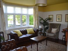 A sitting room with leather sofas, an armchair, a wooden coffee table, lamps, framed pictures, and a large window at Lily House in Minehead