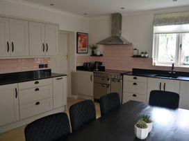 A kitchen with beige cabinets black countertops a stove under a stainless steel hood and a dining table with black chairs and small plants at Lily House in Minehead