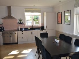 A kitchen with white cabinets black countertop a stainless steel oven a dining table with black chairs and framed pictures on the wall at Lily House in Minehead