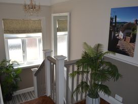 A staircase with wooden railing a large mirror potted plants a window with blinds and a photo on the wall at Lily House Minehead
