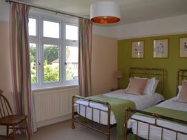 A bedroom with two single beds green throws and pink cushions next to a window with striped curtains at Lily House in Minehead