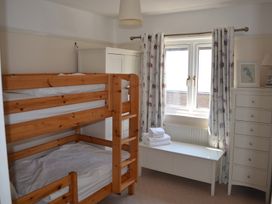 A bedroom with wooden bunk beds a white chest of drawers a white storage bench with towels and a window with patterned curtains at Lily House Minehead