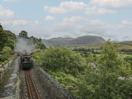 A steam train traveling along tracks surrounded by trees and mountains at Ty Gwynn Tanygrisiau