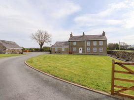 A driveway leading to a two-story house with multiple windows a wooden bench and a stone building with a grassy lawn at Garreg Wen Isaf Bach in Penygroes near Caernarfon