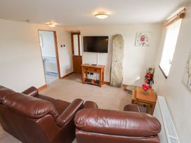 A living room with two brown leather sofas a wall-mounted TV on a wooden table a stone slab a small wooden table with flowers and wall decorations at Garreg Wen Isaf Bach in Penygroes near Caernarfon