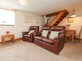 A living room with brown leather sofa and armchair beside wooden staircase and dining table with chairs at Garreg Wen Isaf Bach in Penygroes near Caernarfon