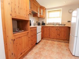 A kitchen with wooden cabinets a white oven a refrigerator and a window with blinds at Garreg Wen Isaf Bach in Penygroes near Caernarfon
