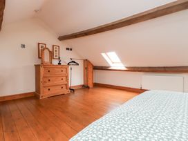 A bedroom with wooden floor beams a wooden dresser a clothes rack and a bed with patterned bedding at Garreg Wen Isaf Bach in Penygroes near Caernarfon
