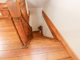 A wooden staircase with banisters and a vase of flowers at the bottom at Garreg Wen Isaf Bach in Penygroes near Caernarfon