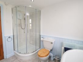 A bathroom with a shower enclosure a toilet with a wooden seat a towel rack with towels and a trash can at Garreg Wen Isaf Bach in Penygroes near Caernarfon