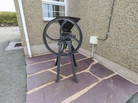 An outdoor area with a vintage metal grinding machine on a stone tiled floor near a rough textured wall at Garreg Wen Isaf Bach in Penygroes near Caernarfon