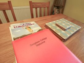 A dining table with a welcome book and coasters at Seaglass Cottage in Aldeburgh
