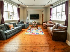 A living room with sofas around a wooden table with flowers a colorful rug and a wall mounted TV at Mountain View in Penmaenmawr