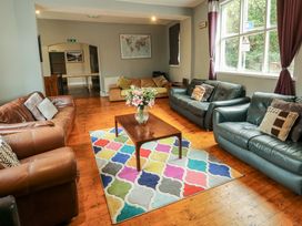 A seating area with multiple sofas a wooden coffee table with a vase of flowers and a colorful patterned rug at Mountain View in Penmaenmawr