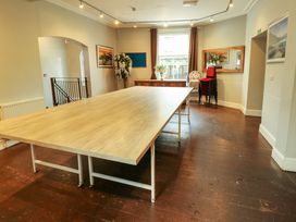 A room with a large wooden table in the center a stack of red chairs a high chair a wooden dresser with flowers and a window behind it at Mountain View in Penmaenmawr
