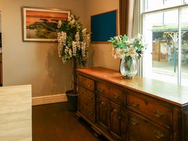A wooden sideboard with a vase of flowers on top next to a potted plant and a window in a room at Mountain View Penmaenmawr
