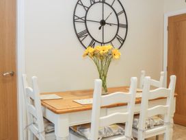 A dining room with a wooden table six white chairs and a vase of yellow flowers with a large wall clock at Lavender Cottage in Market Weighton