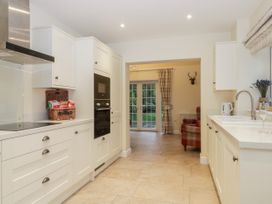 A kitchen with white cabinets an oven a wicker basket and a sink with a window showing a plaid armchair and glass doors at Lavender Cottage in Market Weighton