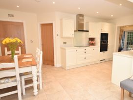A kitchen with white cabinets wooden dining table with chairs and a vase of yellow flowers at Lavender Cottage in Market Weighton