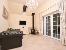 A sitting room with a leather sofa wood burning stove and glass doors with curtains at Lavender Cottage in Market Weighton